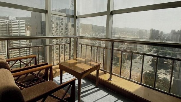 A balcony with a table and chairs, large windows offering a city view.