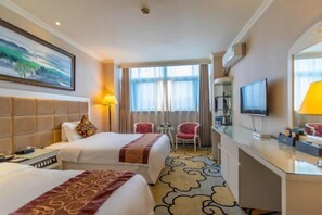 A hotel room with two beds, a desk, a TV, and a window with curtains.