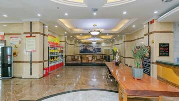 A hotel lobby with a reception desk, seating area, and a large wall with informational posters.