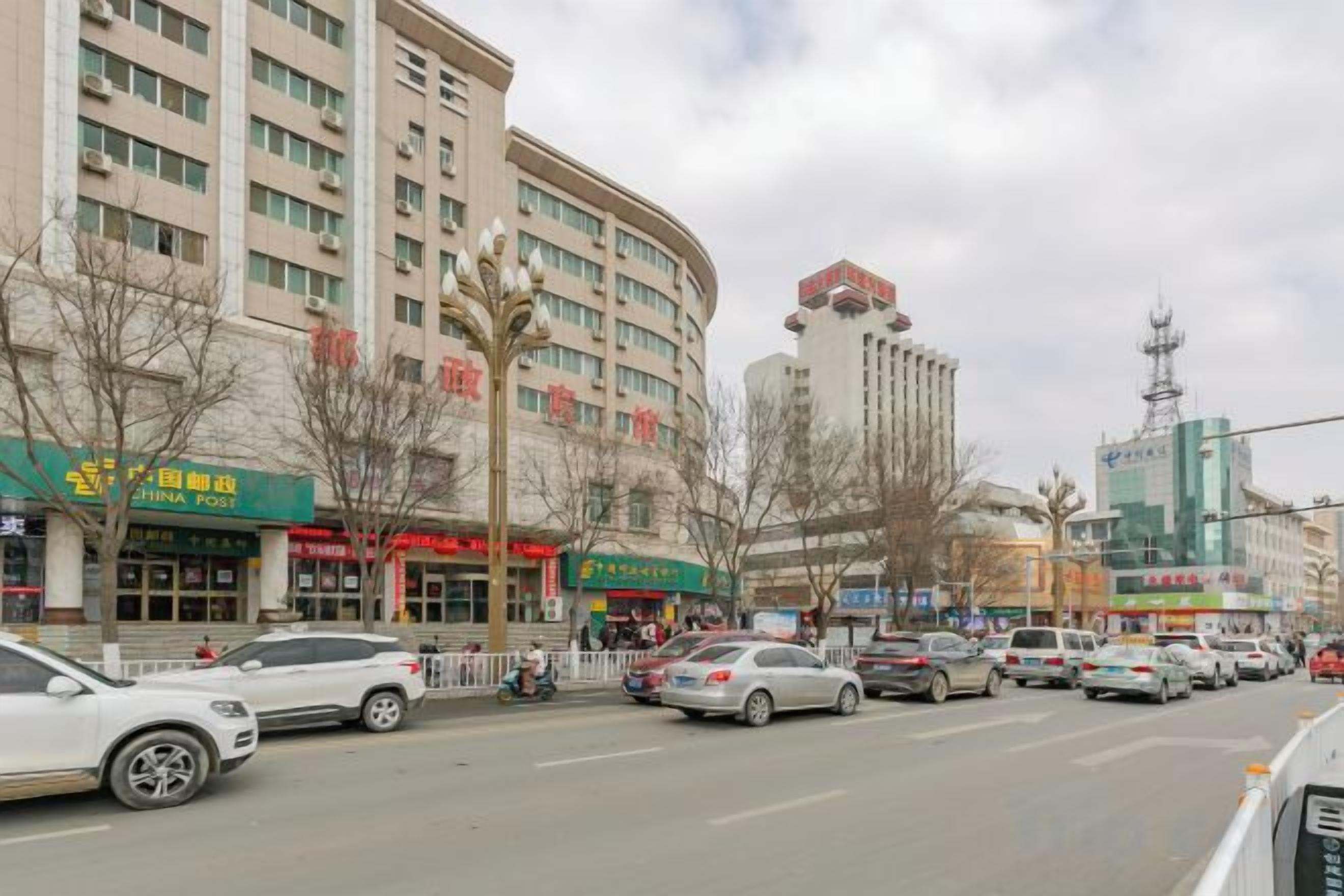 A multi-story building with commercial establishments on the ground floor, a parking lot with several cars, and a clear sky.