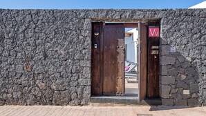 A stone wall entrance with a wooden door, a sign with 'VV' and 'Villa Fae,' and a paved ground.