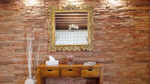 A stone wall with a mirror and a wooden console table with a vase and a tissue box.