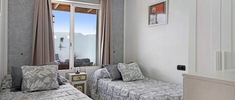 A bedroom with two beds, a window with curtains, a small table, and a wall-mounted picture.