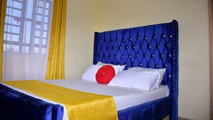 Een bed met een blauw hoofdeinde, wit beddengoed en een gele accentkleur.