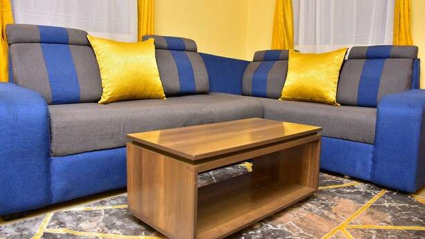 Een modulaire bank met blauwe en grijze kussens en twee gele sierkussens, een houten salontafel en een vloer met een patroon.