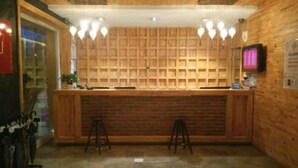 A reception area with a wooden counter, two stools, a digital display, and a brick wall. - Jiuduo Holiday Hotel (Arun Banner)