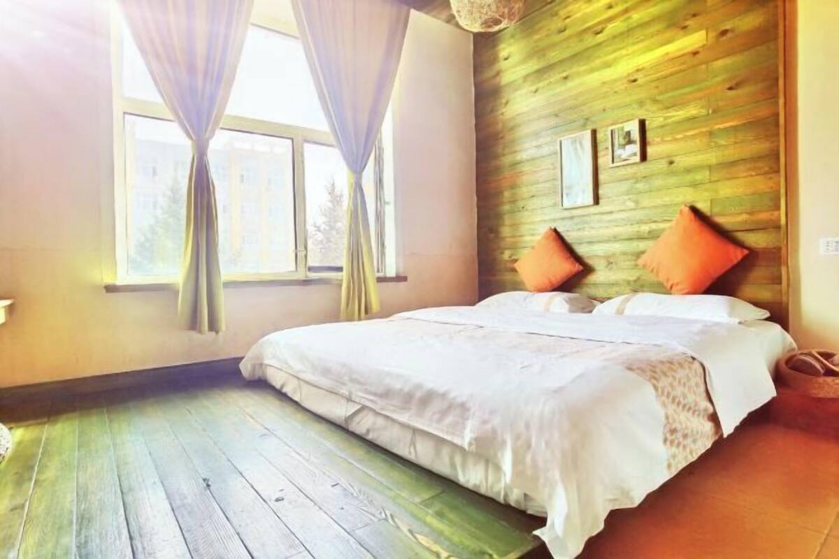A bedroom with a wooden wall, a bed with white bedding, and two orange pillows.