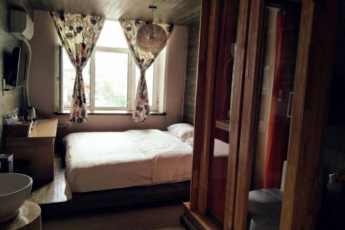A bedroom with a bed, a wooden wardrobe, a bedside table, and a window with curtains.
