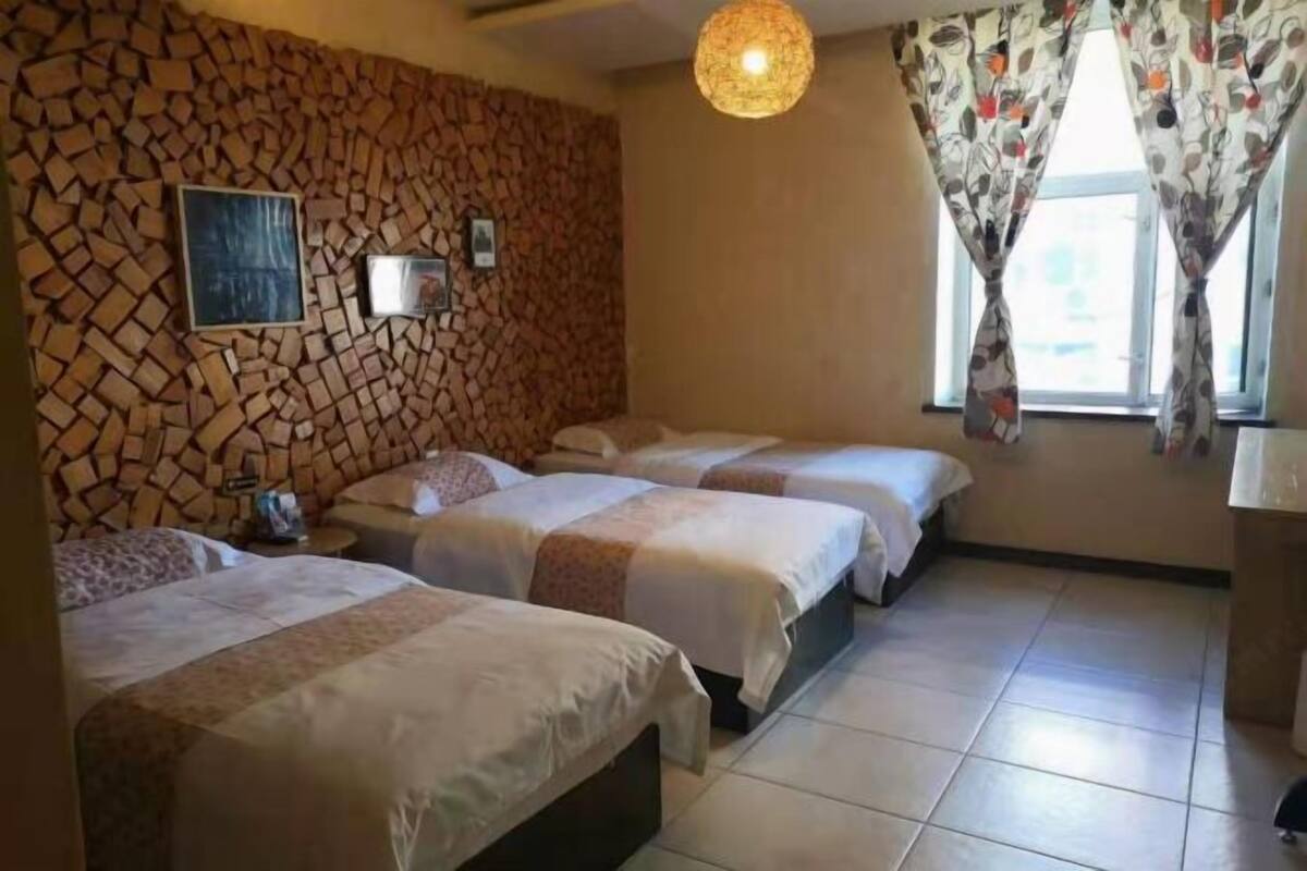 A room with three beds, a stone wall, a hanging light fixture, and a window with curtains.