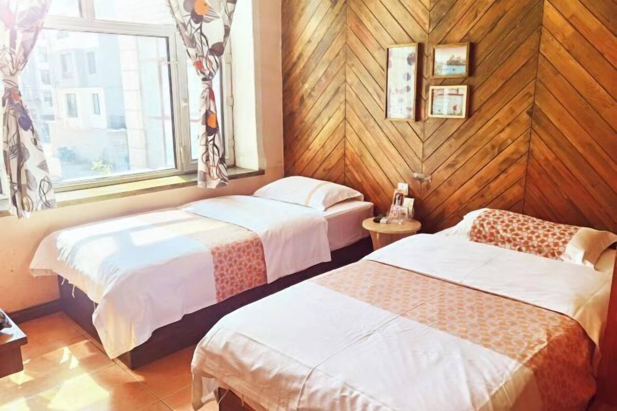 A hotel room with two beds, a wooden herringbone wall, and a window with curtains.