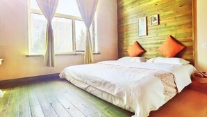 A bedroom with a wooden wall, a bed with white linens, two orange pillows, and a window with curtains. - Jiuduo Holiday Hotel (Arun Banner)
