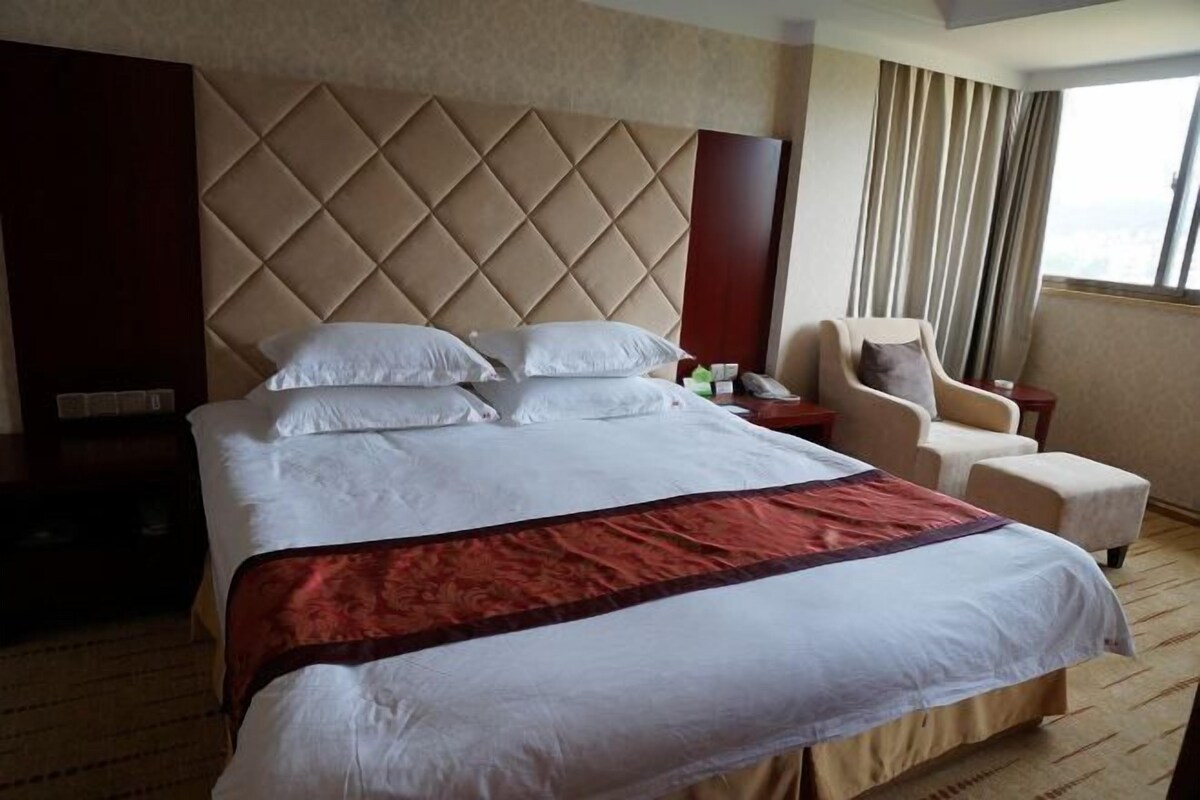 A hotel room with a large bed, a chair, a nightstand, and a view of the city.