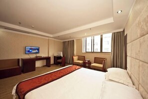 Habitación de hotel con una cama grande, un escritorio con televisor de pantalla plana, dos sillones, una mesita y una ventana con cortinas.