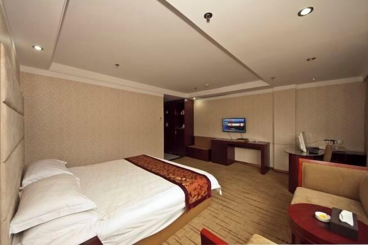 A hotel room with a bed, a desk, a television, and a seating area.