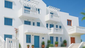 Um edifício branco de vários andares com detalhes em azul, varandas e plantas em vasos.