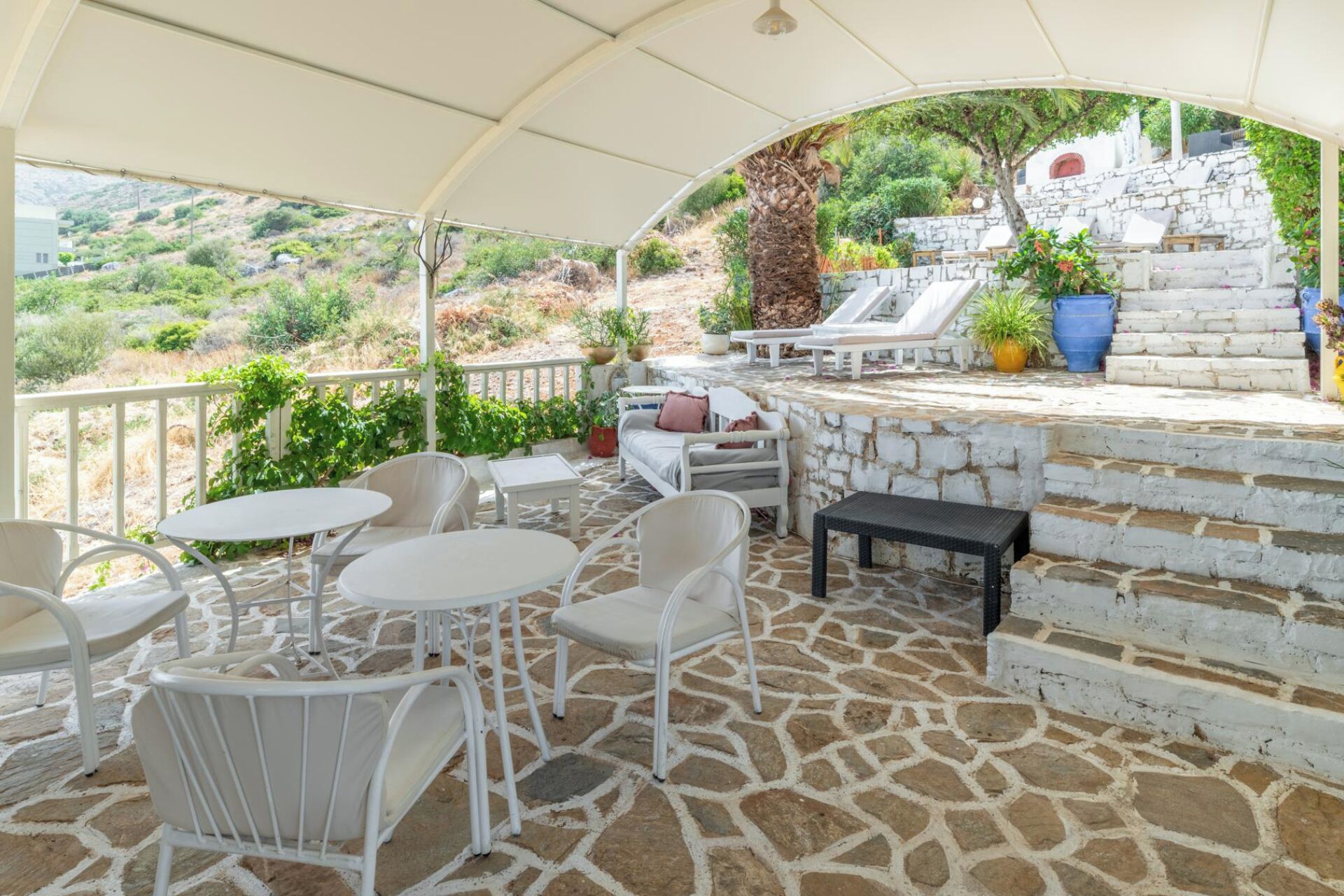 An outdoor patio with white furniture, stone flooring, and a view of a hillside.