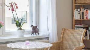 A cozy room with a wicker chair, a small table, a bookshelf, and a window with a view.