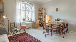 A cozy living room with a dining area, a bookshelf, and a window with curtains.