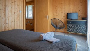 Een kamer met houten lambrisering, een bed, een stoel, een dressoir en een televisie.
