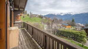 Een houten balkon met uitzicht op een bergachtig landschap en huizen.
