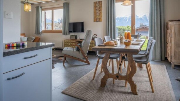 Een moderne keuken met een eethoek, houten balken, een flatscreen-tv en uitzicht op bergen.
