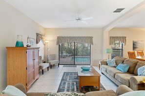 A spacious living room with a sofa, a coffee table, a cabinet, and a view to a balcony. - CHARMING OASIS VILLA NEAR DISNEY WITH POOL, BBQ, AND OUTDOOR ADVENTURES (Clermont)