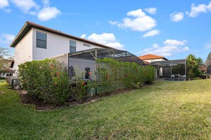 A house with a covered patio area, a lawn, and a garden with flowering plants. - CHARMING OASIS VILLA NEAR DISNEY WITH POOL, BBQ, AND OUTDOOR ADVENTURES (Clermont)
