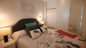 Hotelkamer met een groot bed, een hoofdbord, nachtlampjes, een decoratief wandobject en een badkamer zichtbaar door een glazen scheidingswand.