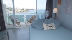 Een hotelkamer met een bed, twee stoelen, een tafel en uitzicht op de zee en gebouwen.