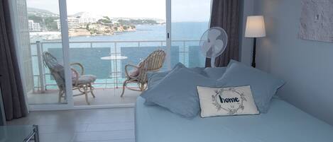 Habitación de hotel con cama, dos sillas, una mesa y vistas al mar y edificios.