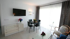Een moderne woonkamer met een flatscreen televisie, een eethoek met stoelen en een tafel, een bank en een klein bijzettafeltje met een bloevas.