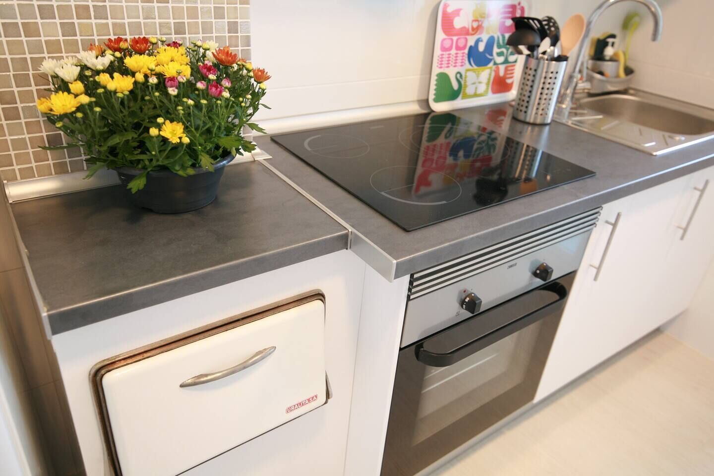 A kitchen with a stainless steel countertop, a built-in oven, and a white cabinet with a handle.