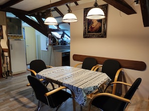 A dining area with a table covered in patterned tablecloth, surrounded by chairs with wooden frames and black cushions. There are two pendant lights hanging above the table. A framed picture is visible on the wall above the table. - Family -ONLY- welcome to Berching (Berching)