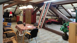 Una habitación acogedora en el ático con una mesa de comedor, sillas, un sofá y una escalera.
