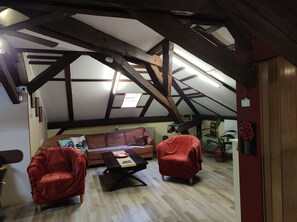 A loft-style room with exposed wooden beams, a brown leather sofa, two red armchairs, and a wooden coffee table. - Family -ONLY- welcome to Berching (Berching)