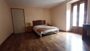 A bedroom with a wooden floor, a bed with a floral bedspread, a nightstand with a lamp, and a door. - Apartment by the river with snow peak views (Modane)