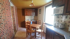 A compact kitchen with a dining area, wooden cabinets, a microwave, and a hanging light fixture. - Apartment by the river with snow peak views (Modane)