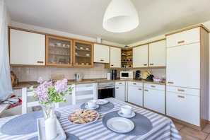 Uma cozinha moderna com armários brancos, micro-ondas, máquina de café e uma mesa de jantar posta com pratos e um vaso de flores.