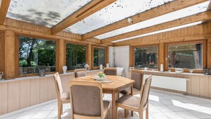 Ein Zimmer mit Holzwänden, einem großen Tisch und Stühlen, großen Fenstern und Blick ins Freie.