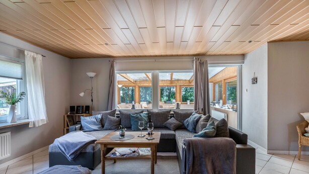 Ein modernes Wohnzimmer mit Holzboden, einer Sofagarnitur, einem Couchtisch und großen Fenstern.