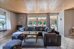 Un salon moderne avec un plafond en bois, un ensemble de canapés, une table basse et de grandes fenêtres.