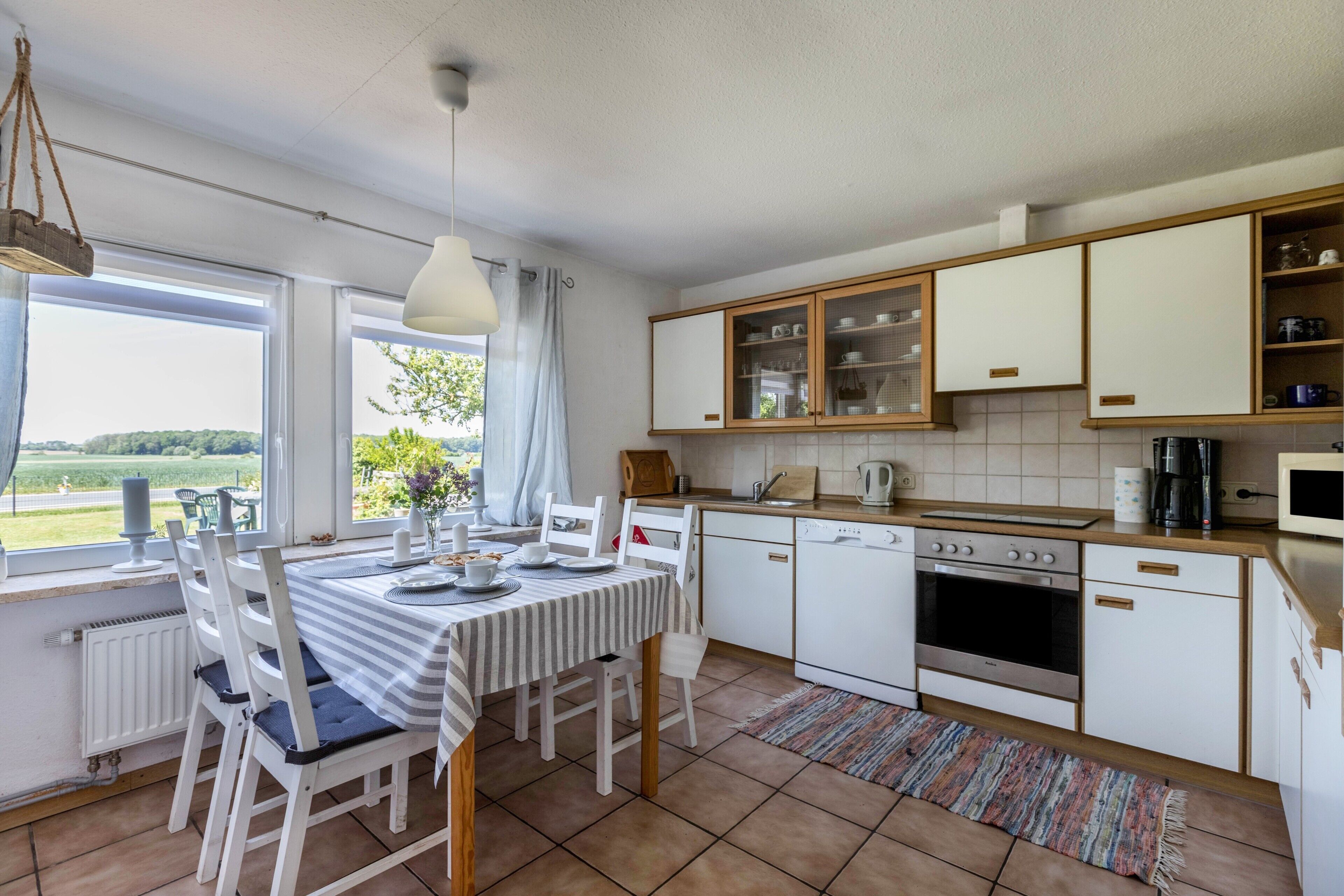 Uma cozinha com armários brancos, uma mesa de jantar com cadeiras, uma janela com vista e um pendente.