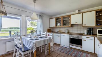 Uma cozinha com armários brancos, uma mesa de jantar com cadeiras, uma janela com vista e um pendente.