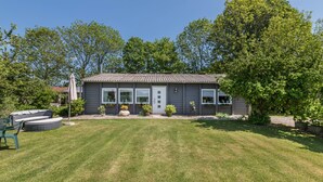 Ein eingeschossiges Haus mit Veranda, Rasen und einem großen Baum zur Rechten.