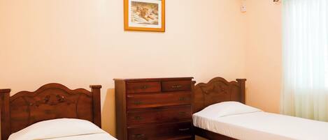 A bedroom with two single beds, a wooden dresser, a framed picture on the wall, and an air conditioning unit.