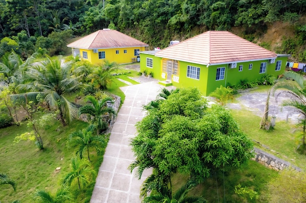 A green and yellow house with a red roof, surrounded by lush greenery and a stone pathway. - Tranquil Retreat Vacation Home (Tower Isle)