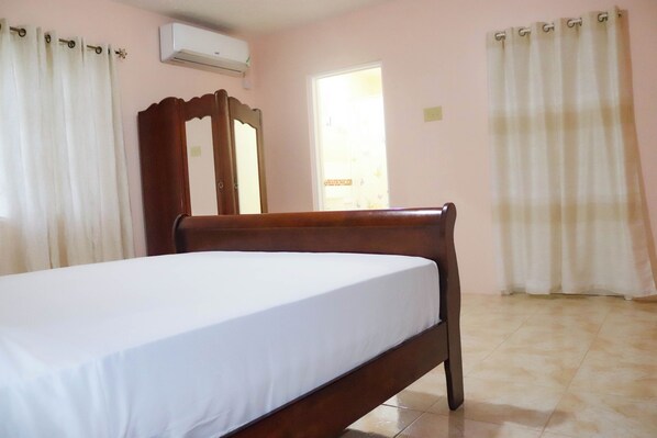 A single bed with a wooden frame and white bedding in a room with pink walls, a window, and curtains. - Tranquil Retreat Vacation Home (Tower Isle)