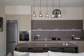 A modern kitchen with a central island, stainless steel appliances, pendant lighting, and a clock on the wall.