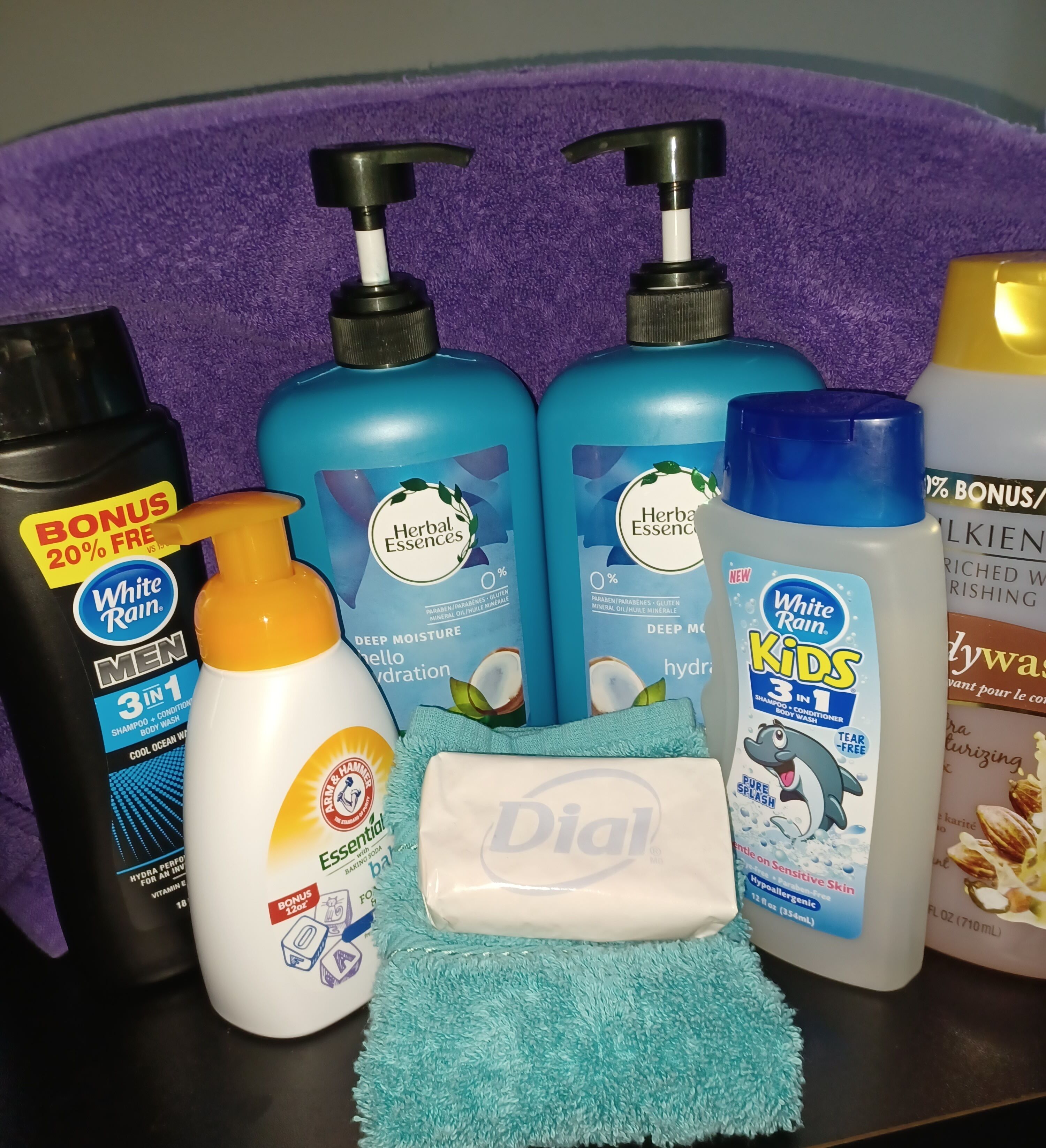 A variety of personal care products including shampoos, conditioners, and body wash on a purple towel.