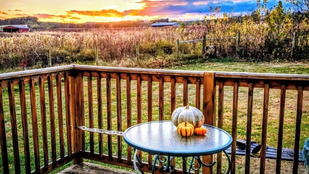 Eine Holzdar Terrasse mit Tisch und Stühlen, mit Blick auf ein Feld und einen Sonnenuntergang.